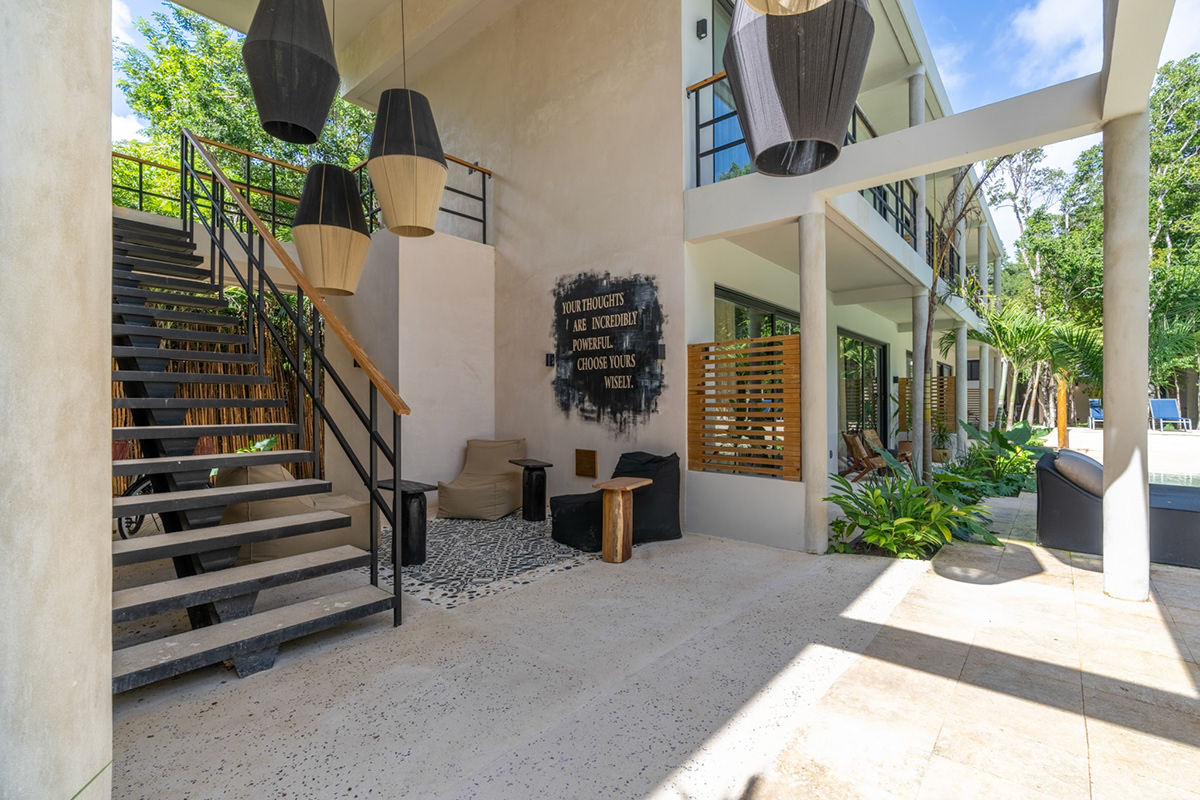 Open-air entrance with stairs, hanging lights, and planted seating — Attha
