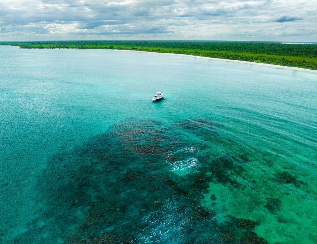 Aerial view of a yacht on clear turquoise water near the coastline — Jungle Luxe Yacht