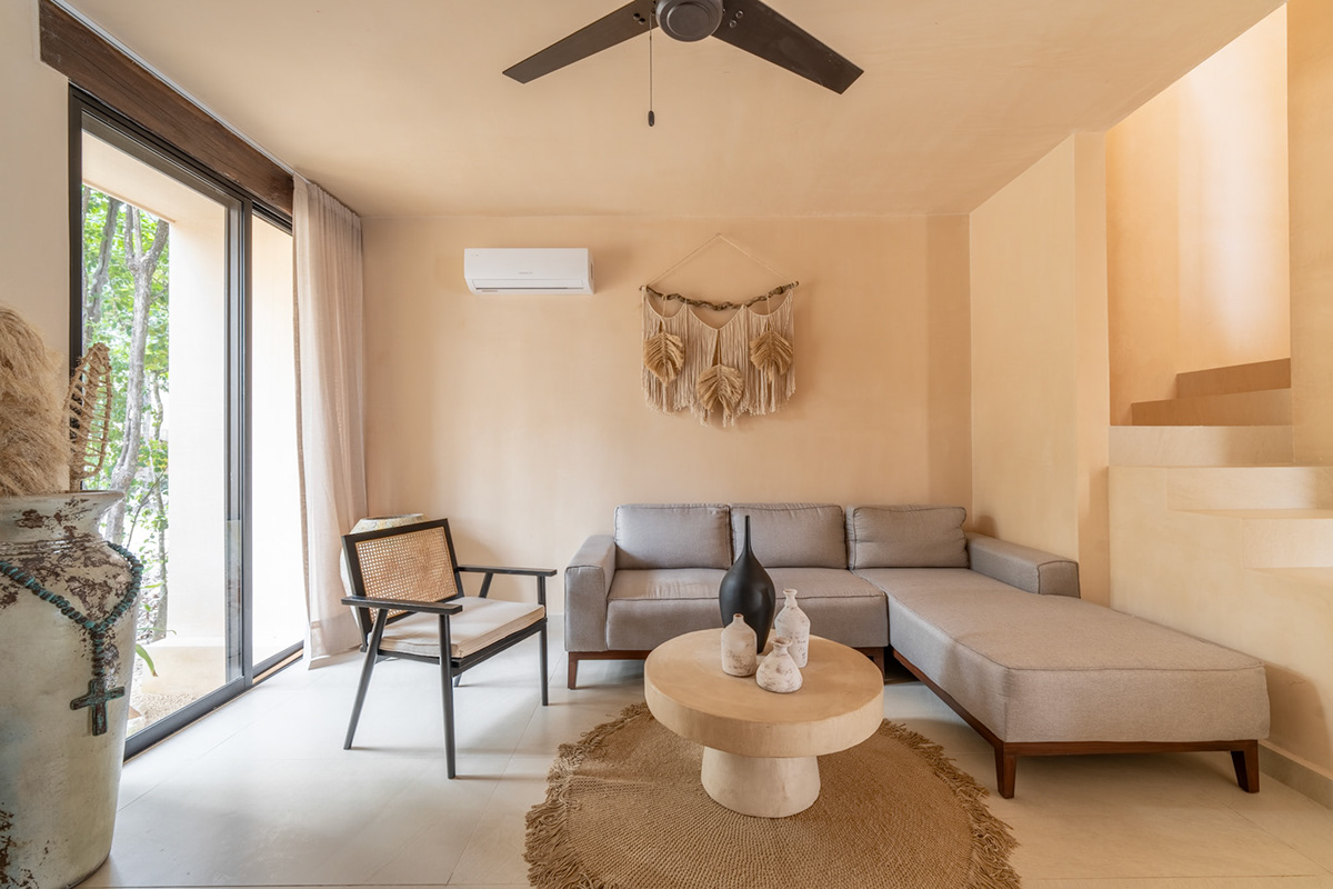 Living room with a gray sectional, round timber table, and garden-facing windows — Surenna 21